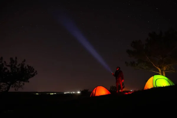 キャンプ場のテントの近くに明るい懐中電灯を持つ男は夜に屋外 — ストック写真