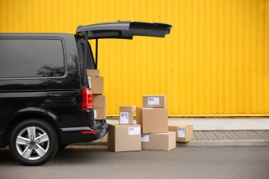 Siyah teslimat minibüsü ve sarı binanın yakınında bir sürü farklı paket var. Mesaj için yer var. Kurye servisi