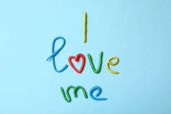 Phrase I Love Me made of modelling clay on light blue background, flat lay
