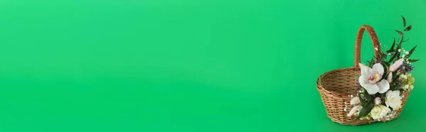 緑の背景に美しい花で飾られたウィッカーバスケット テキストのためのスペース イースターアイテム — ストック写真