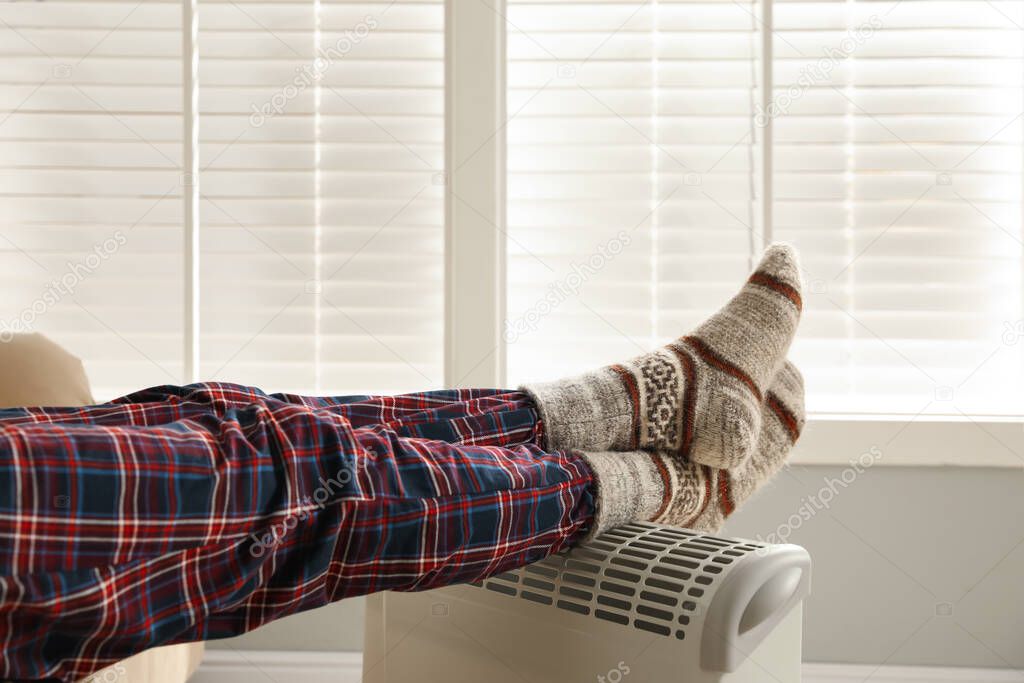 Man warming feet on electric heater at home, closeup