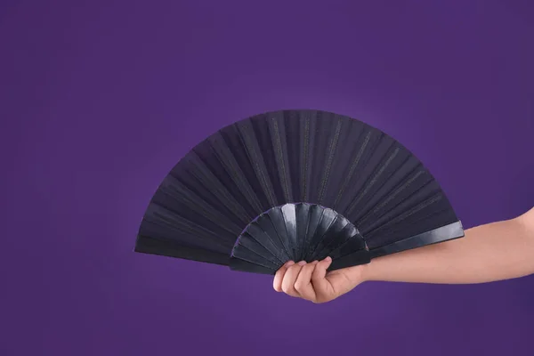 Woman holding black hand fan on purple background, closeup