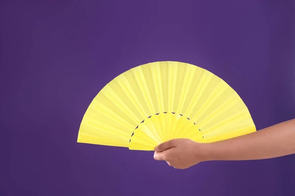 Woman holding yellow hand fan on purple background, closeup
