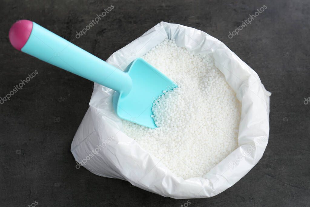 Bag with granular mineral fertilizer and scoop on grey background, top view
