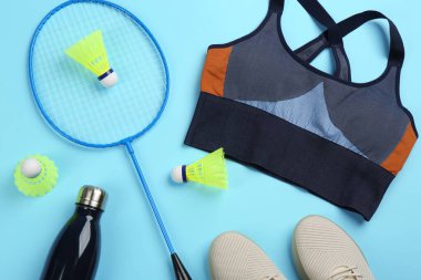 Raketler, spor kıyafetleri ve açık mavi arka planda şişe, düz yatış. Badminton oynuyorum.