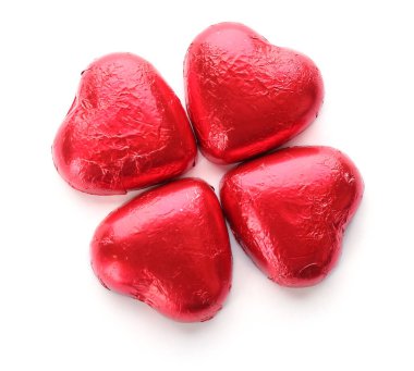 Kalp şeklinde çikolata şekerlemeleri kırmızı folyoyla beyaz arka planda, üst görünümde.