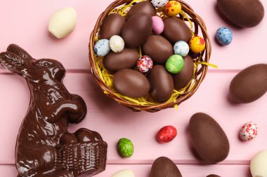 Çikolatalı Paskalya tavşanı ve pembe ahşap masanın üzerinde yumurtalar.