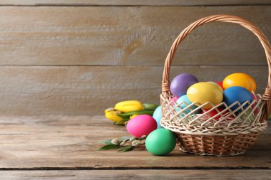 Hasır sepetteki renkli Paskalya yumurtaları ahşap arka planda. Metin için boşluk