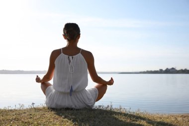 Gün batımında nehrin kenarında meditasyon yapan genç bir kadın. Doğa iyileştirme gücü