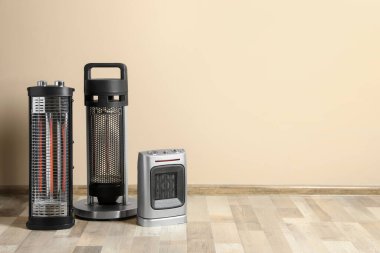 Different modern electric heaters on floor in room, space for text clipart