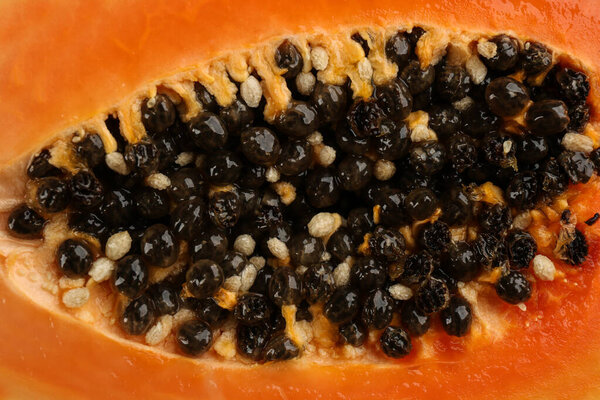 Fresh cut papaya fruit with black seeds as background, closeup view