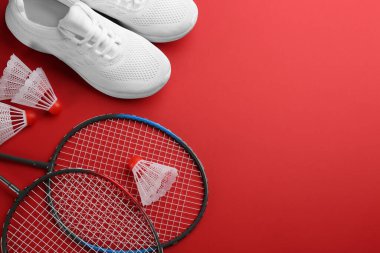 Badminton raketleri, mekik penisleri ve kırmızı arka planda ayakkabılar, düz yatış. Metin için boşluk