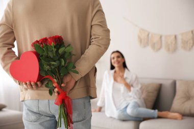 Güzel bir buketi ve hediye kutusunu evinde arkasına saklayan bir adam, yakın plan. Sevgililer Günü kutlaması