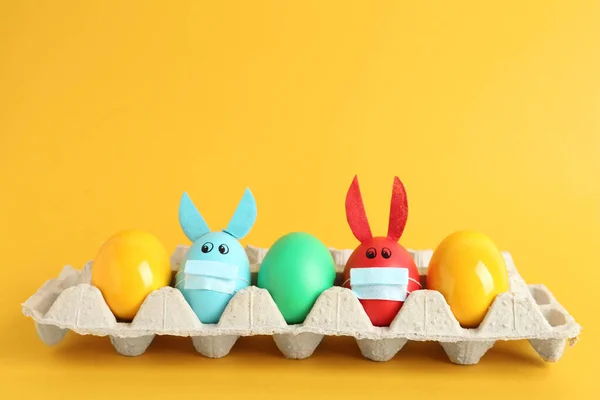 彩绘鸡蛋 用兔子耳朵装饰 保护膜包裹在黄色的背景上 Covid 19检疫期间的复活节假期 — 图库照片