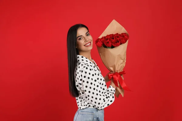 赤い背景にチューリップの花束を持つ幸せな女性 3月8日 — ストック写真