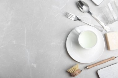 Gri arkaplan üzerinde sofra takımı ve temizlik fırçası olan düz bir kompozisyon, metin için boşluk. Bulaşık malzemeleri.