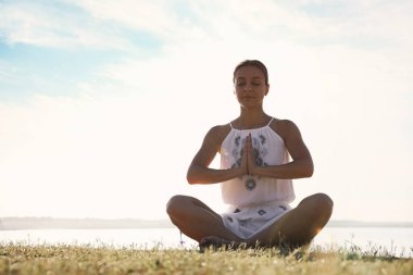 Gün batımında nehrin kenarında meditasyon yapan genç bir kadın. Doğa iyileştirme gücü