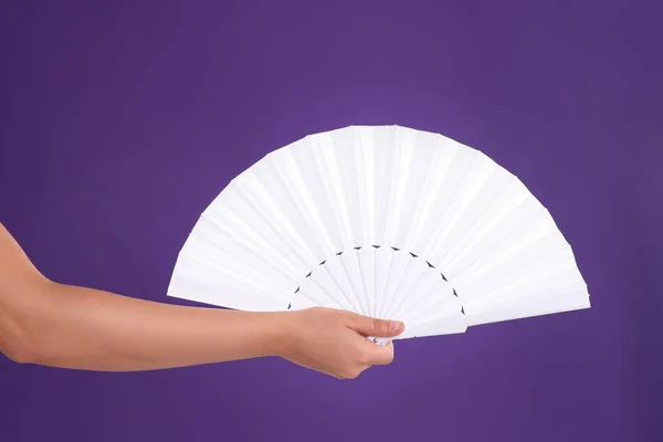 Woman holding white hand fan on purple background, closeup