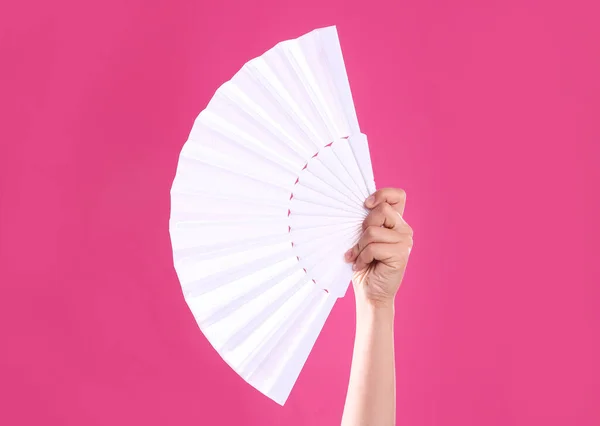 Woman holding white hand fan on pink background, closeup
