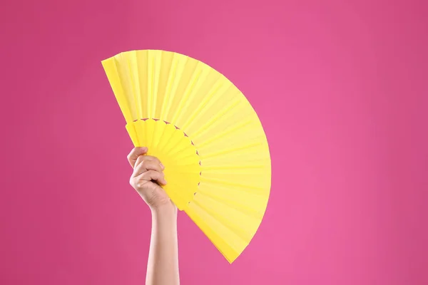 Woman holding yellow hand fan on pink background, closeup