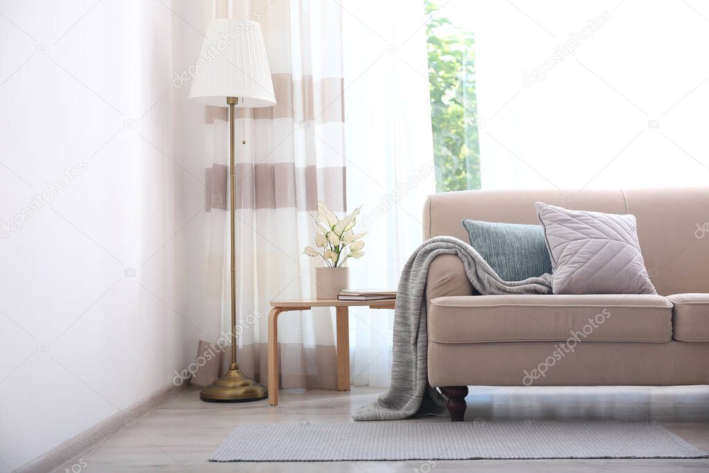 Comfortable sofa near window with stylish curtains in living room. Interior design