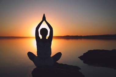 Gün batımında nehir kenarında yoga yapan bir kadın. İyileştirme kavramı