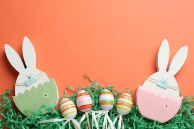 Koruyucu maskeli ahşap tavşanlar, mercan arka planda yazı yazmak için yumurtalar ve boşluk, düz yatış. COVID-19 karantinasında Paskalya tatili