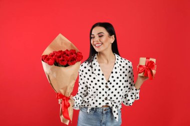Kırmızı arka planda lale buketi ve hediye kutusu olan mutlu bir kadın. 8 Mart kutlamaları