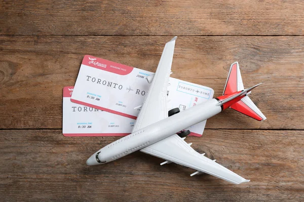 Toy airplane with tickets on wooden background, flat lay