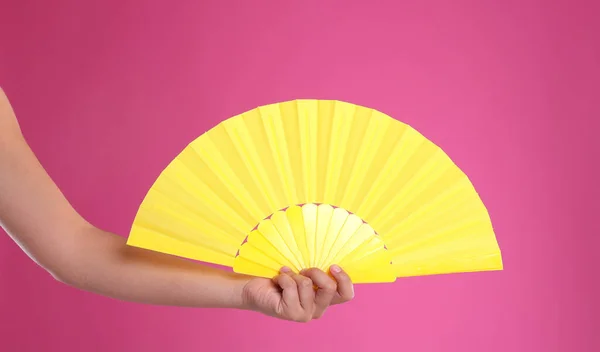 Woman holding yellow hand fan on pink background, closeup