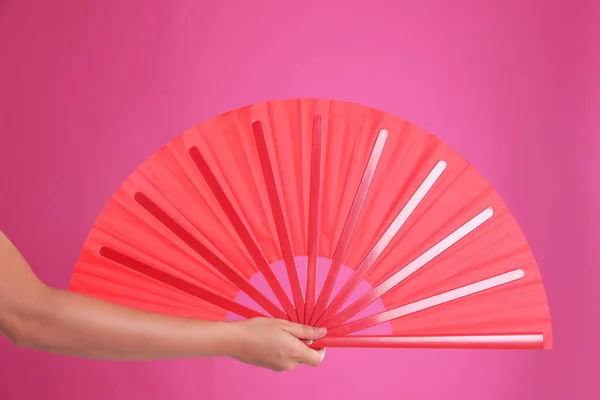 Woman holding red hand fan on pink background, closeup