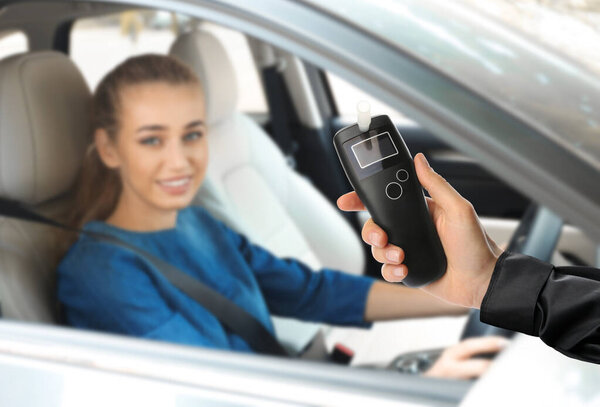 Police officer with breathalyzer and woman in car. Alcohol consumption while driving