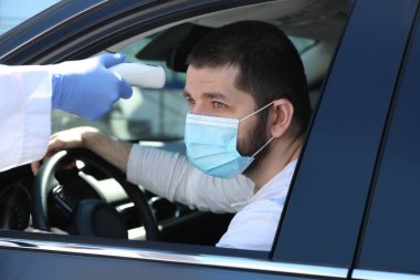 Doktor, dışarıda temas olmayan kızılötesi termometreyle sürücü sıcaklığını ölçüyor.