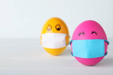 Beyaz ahşap masada koruyucu maskeli parlak yumurtalar, yazı için yer. Coronavirus karantinası sırasında Paskalya tatili