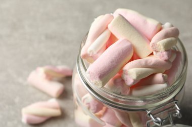 Açık gri masada leziz marşmelovlarla dolu cam kavanoz, yakın plan. Metin için boşluk