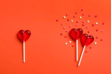 Düz kompozisyon, tatlı kalp şekilli lolipoplar ve mercan zemin üzerine serpiştirilmiş şekerlemeler. Aşk üçgeni kavramı
