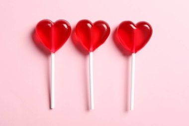 Tatlı kalp şeklinde lolipoplar pembe arka planda, düz yerde. Sevgililer Günü kutlaması
