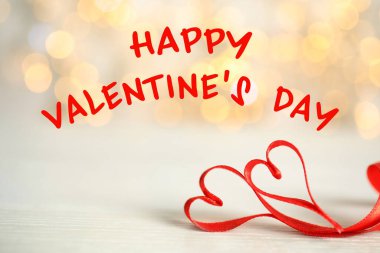 Sevgililer Günün kutlu olsun. Masadaki bulanık ışıklara karşı kırmızı kurdeleden yapılmış iki kalp 