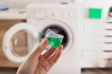 Çamaşır makinesinin yanında çamaşır deterjanı kapsülü tutan kadın.