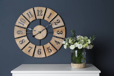 Gri duvarın yanındaki beyaz masada vazoda güzel Eustoma çiçekleri olan bir buket.