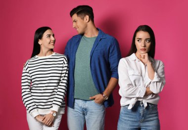 Mutlu olmayan kadın kıskanırken çift pembe arka planda birlikte vakit geçiriyor.