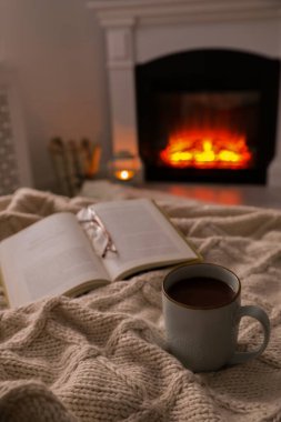 Evdeki şöminenin yanında bir fincan sıcak çay, gözlük ve kitap. Sıcak atmosfer