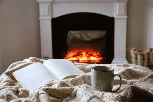 Cup of hot tea and book near fireplace at home. Cozy atmosphere