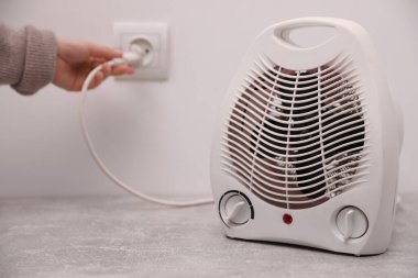 Kadın elektrikli fan ısıtıcısını içeri takıp cihaza odaklanıyor. Metin için boşluk
