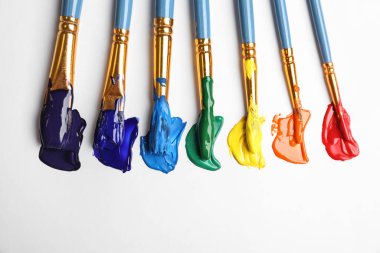 Beyaz arka planda farklı boyalarla fırçalar, düz bir zemin. Gökkuşağı renkleri