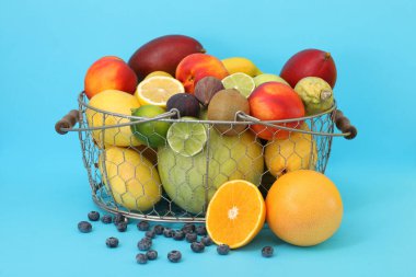 Açık mavi arka planda sepette taze egzotik meyveler var.