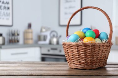 İçerideki ahşap masada parlak boyalı Paskalya yumurtalarıyla dolu Hasır sepet. 