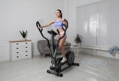 Evdeki eliptik makinede eğitim gören mutlu genç kadın.