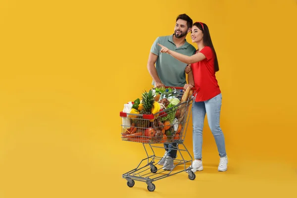 Sarı Arka Planda Alışveriş Arabasıyla Alışveriş Yapan Genç Çift — Stok fotoğraf