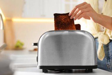 Mutfaktaki tost makinesinden yanmış ekmeği alan kadın.